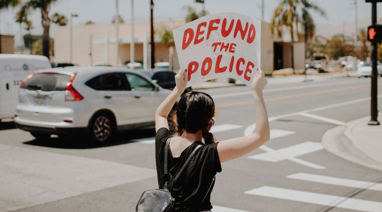 woman holding defund the police banner