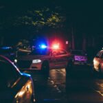 Police cars parked on a dimly lit street at night, their lights flashing in the darkness, creating a scene of vigilance.