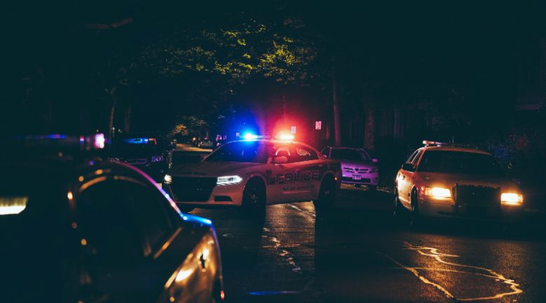 Police cars parked on a dimly lit street at night, their lights flashing in the darkness, creating a scene of vigilance.