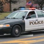 A police car drives down the street, proudly displaying an American flag on its rear.