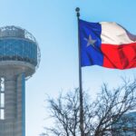 Texas flag waving in front of the iconic Dallas tower, symbolizing the state's pride and urban landscape.