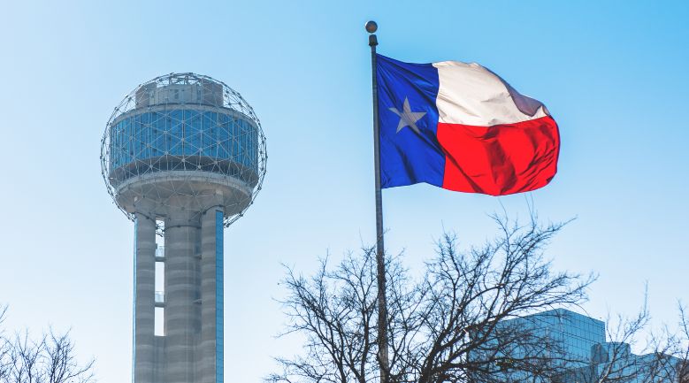 Texas flag waving in front of the iconic Dallas tower, symbolizing the state's pride and urban landscape.